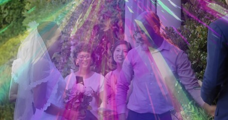 Walking bride wearing wedding gown and veil holding bouquet on garden pathway, guests smiling