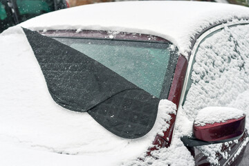 Winter windshield cover protecting parked car from frost and ice on cold morning, illustrating difference between covered and uncovered surface.