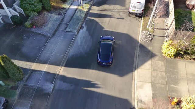 Aerial view of a blue electric car driving through a suburban neighborhood and arriving at a home