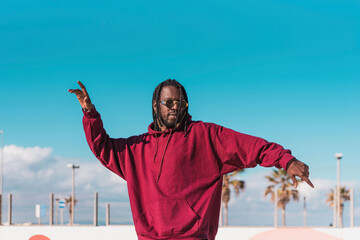 African American man in sunglasses and dreadlocks dancing on street against blue sky © Renata Hamuda