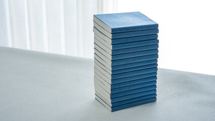 明るい室内のテーブルの上に高く積み上げられた青いブックカバーの文庫本