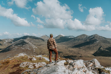A hiker stands atop a rugged quartzite peak in Connemara National Park, surveying the dramatic Twelve Bens mountain range under a vast, cloud-filled sky. © Agnieszka Gaul