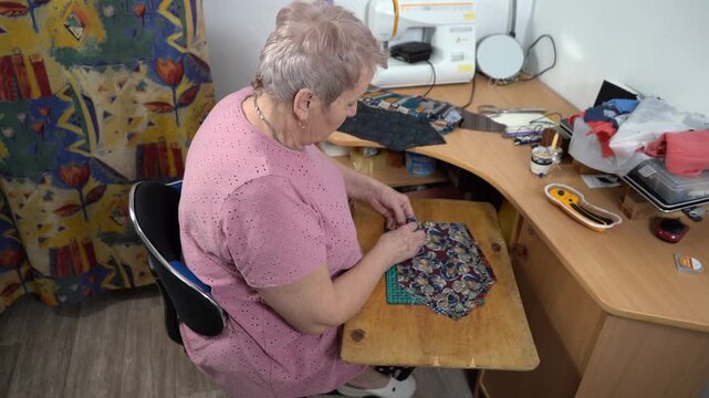 Elderly woman sew a patchwork quilt. Needlework sewing.