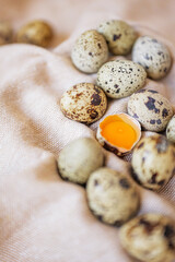 Obraz premium Quail eggs and one cracked egg with yolk on soft surface in simple setting