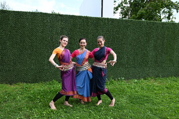 Obraz premium Three dancers in national costumes dance in the park on a summer day. Indian dance lessons, choreography.