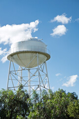Water tower stands tall against a bright blue sky with clouds and trees