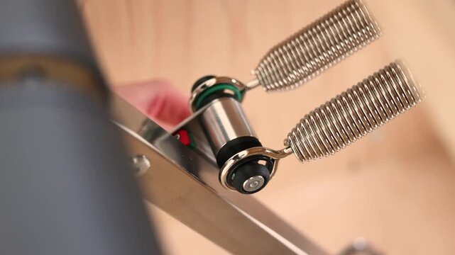 Detailed close up of metal springs in motion on pilates reformer training machine. Visible tension and mechanical movement during exercise demonstrates functionality engineering and precision 