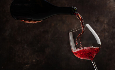 Fototapeta premium Pouring red wine into the glass on rustic dark background. Pour alcohol, winery concept.