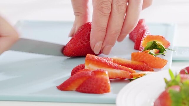 Woman slices strawberries on a cutting board using a knife with a pink handle. High quality 4k footage
