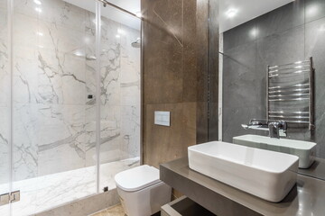 A bright residential bathroom features a glass shower, a modern sink, and tiled walls. Natural light fills the space, highlighting the design and fixtures present