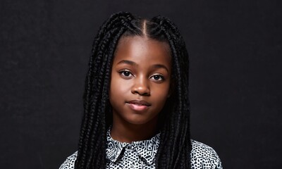 Young girl with braided hair poses calmly in front of a dark background in a studio setting during a portrait session