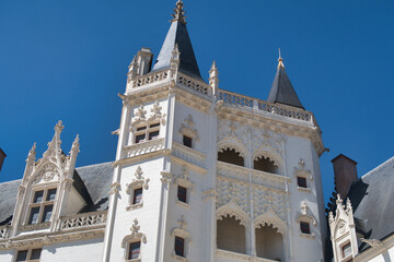 Ornate Renaissance Chateau Turrets - Close-up of a white stone French chateau facade with intricate Renaissance carvings and sharp, dark slate roofs on corner turrets against a blue sky. © jmag.foto