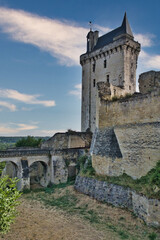 Obraz premium Medieval Castle Ruins and Stone Keep - Ancient medieval castle ruins and fortifications with a dominating stone keep tower under a dramatic blue, cloudy sky in the Loire Valley.