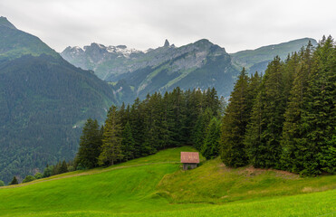 Scenic view of Lauterbrunnen Valley featuring a traditional alpine cabin surrounded by green meadows, steep cliffs, and waterfalls in Switzerland