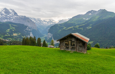 Obraz premium Scenic view of Lauterbrunnen Valley featuring a traditional alpine cabin surrounded by green meadows, steep cliffs, and waterfalls in Switzerland