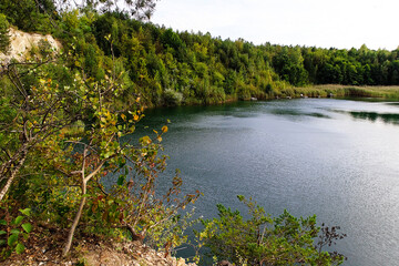 Fototapeta premium Panoramic view of a calm lake surrounded by green forest, natural scenery ideal for travel and nature themes.