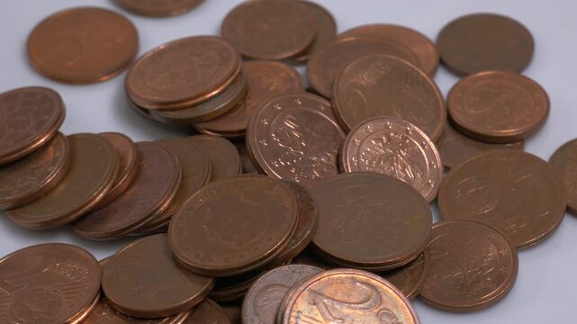 A pile of Euro cent coins scattered on a white plate, rotating slowly in a studio setting to showcase the fine details and engravings of the currency.