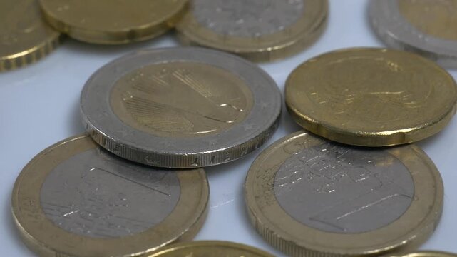 A variety of Euro coins scattered on a white plate, rotating slowly in a studio environment to highlight their metallic textures and intricate currency designs.