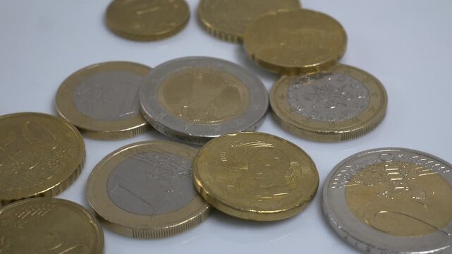 A variety of Euro coins scattered on a white plate, rotating slowly in a studio environment to highlight their metallic textures and intricate currency designs.
