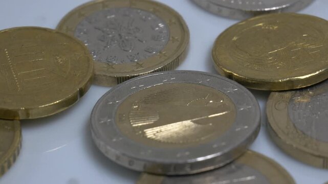 A variety of Euro coins scattered on a white plate, rotating slowly in a studio environment to highlight their metallic textures and intricate currency designs.