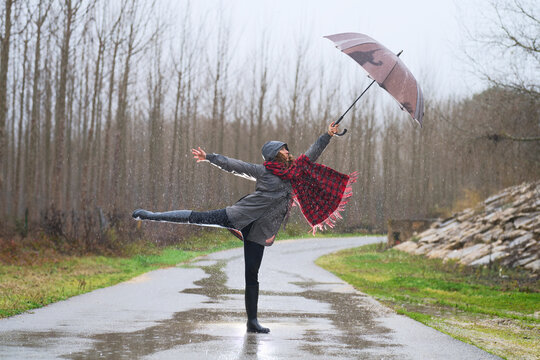 Woman joyfully dancing in the rain with an umbrella
