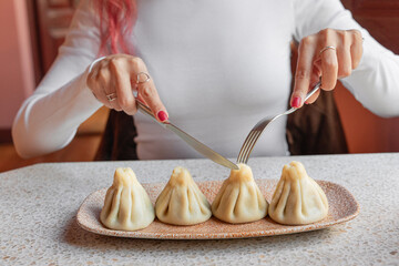 Woman poised with fork and knife over steaming plate of fresh khinkali dumplings in cozy Georgian restaurant, ready to eat