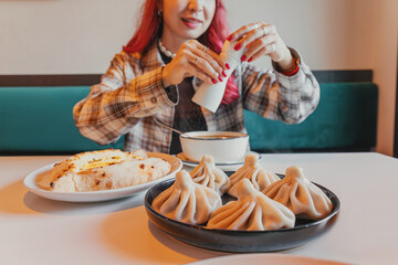 Young woman adding seasoning to her soup while eating a traditional Georgian meal with khinkali dumplings and khachapuri