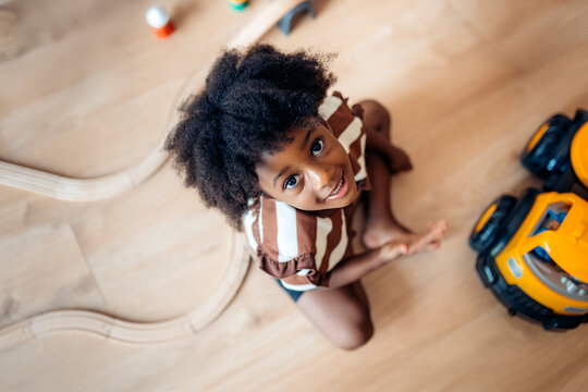 Child playing happily on a wooden floor with toy cars