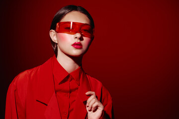 Stylish woman in bold red fashion outfit poses against a red background wearing futuristic tinted...