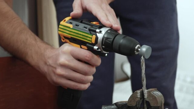 Hands of caucasian man with power drill sharpening drill bit in vise using attachment grinding stone closeup. Restoring functionality of metal cutting tool.
