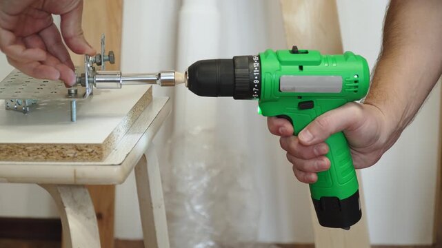 Hands of caucasian man with cordless impact wrench tightening nuts on homemade device closeup. Using wireless tool with lighting to fasten metal parts.