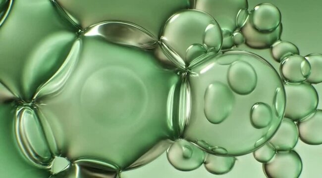 Extreme close-up of translucent green liquid bubbles and oil droplets creating a complex geometric pattern.