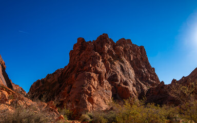 Dramatic red rock canyon peak under a vivid blue sky, sunlit sandstone cliffs and desert scrub&mdash;perfect for hiking, photography, and outdoor adventure.