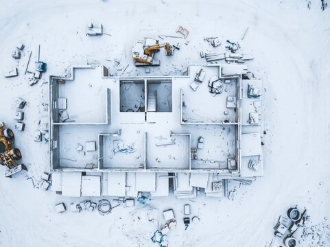 A top-down architectural view of a building floor plan covered in snow, with construction tools scattered around, symbolizing planning, architecture, renovation, and winter construction.