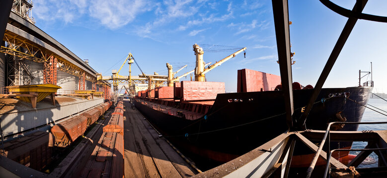 Industrial port terminal loading a cargo ship with heavy cranes and freight trains