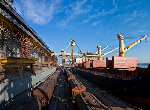 Industrial port terminal loading a cargo ship with heavy cranes and freight trains