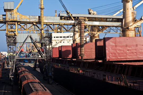 Industrial port terminal loading a cargo ship with heavy cranes and freight trains