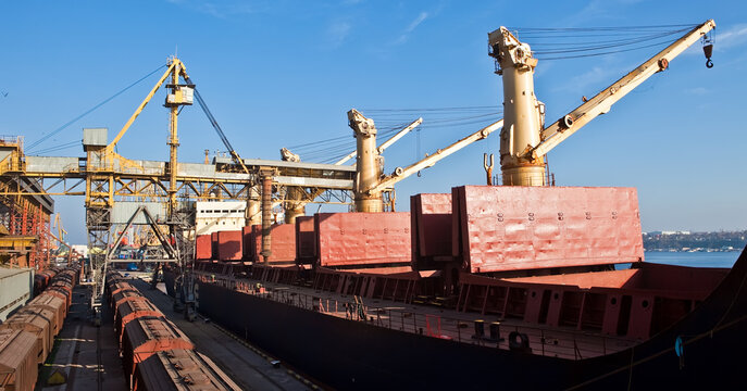 Industrial port terminal loading a cargo ship with heavy cranes and freight trains