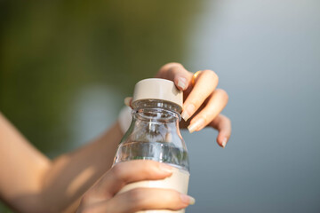 A close-up shot of a person unscrewing a bottle cap in a natural setting by the water.