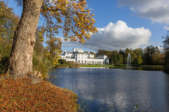 Soestdijk Palace reflected in the calm waters of the Baarn lake on a sunny autumn day with colorful leaves