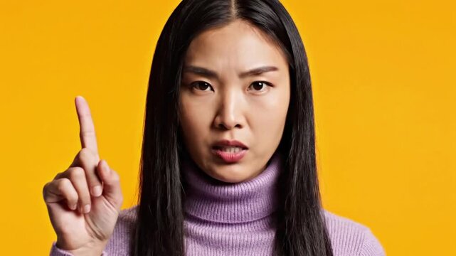 Woman speaks in front of bright orange background while raising one finger to emphasize a point about communication