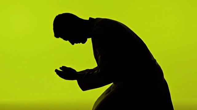 Silhouette of a devout man kneeling in prayer and worship.