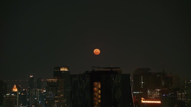 Luminous blood moon seta over modern Bangkok cityscape at night with illuminated skyscrapers rooftops and city lights