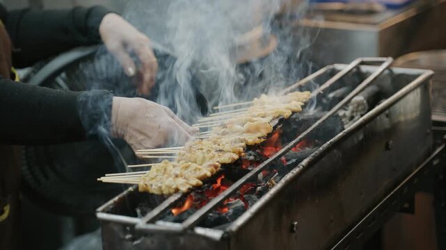 Street food vendor grills traditional pork satay skewers over a charcoal fire at a night market in Bangkok, Thailand