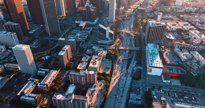 Flight over the modern multi-lane highways with a crazy traffic in the metropolis. Los Angeles downtown, California, US at sunset time.