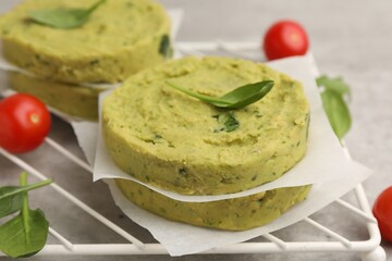Uncooked chickpea patties with spinach and tomatoes on gray table, closeup