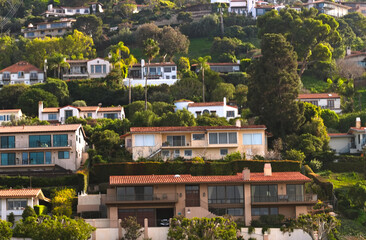 Fototapeta premium Hillside homes overlook Torrance Beach, California, showcasing Mediterranean architecture, dense greenery, and sunlit coastal living.