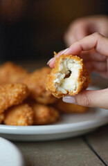 Close up of hand holding a crispy fried chicken bite. Juicy chicken tenders served on a white plate. Delicious fast food item ready for consumption at a casual eatery.