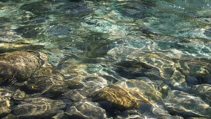Obraz premium The clear turquoise water ripples over the riverbed stones creating a dazzling display of light and shadow in a natural and mesmerizing water scene.