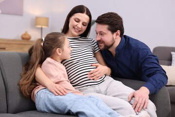 Fototapeta premium Pregnant woman, her husband and daughter on sofa at home